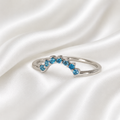 Sterling silver curved crown stacker ring with blue topaz crystals on white satin