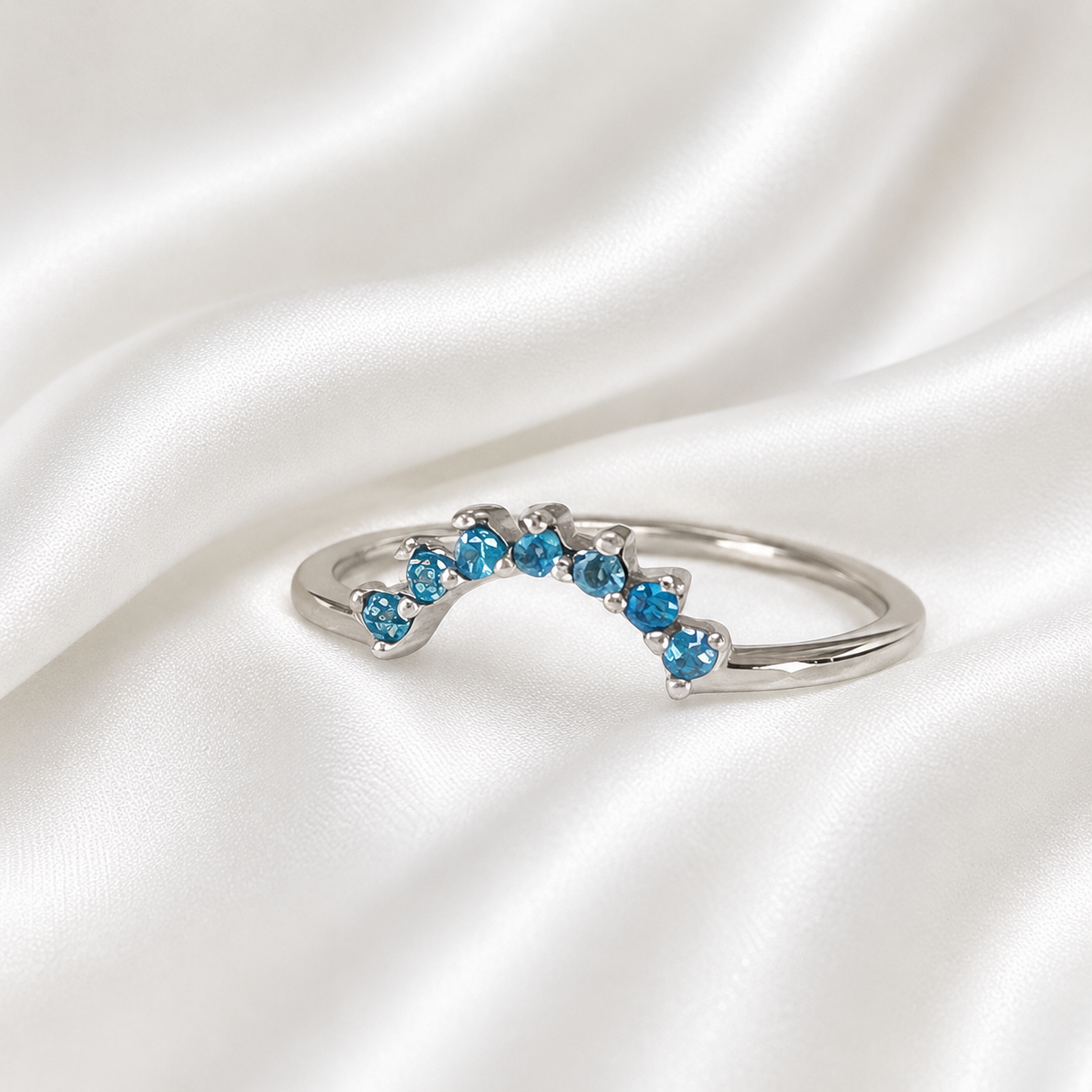 Sterling silver curved crown stacker ring with blue topaz crystals on white satin