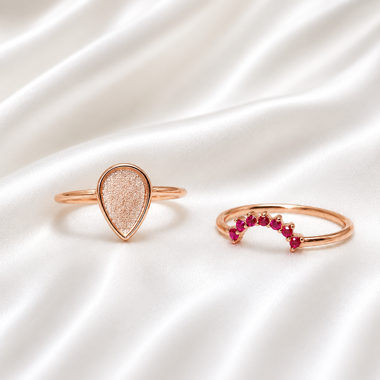 Rose gold teardrop ring set with ruby red birthstone stacker band on white satin
