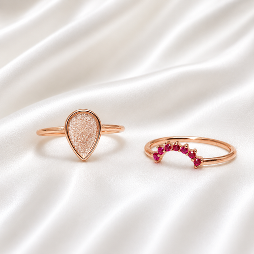 Rose gold teardrop ring set with ruby red birthstone stacker band on white satin