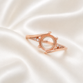 Rose gold 925 sterling silver round open bezel split shank ring setting with CZ accents on cream satin - angle view